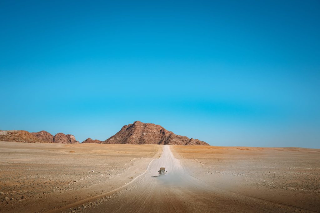 Auto auf shotterpiste fährt vor Berg in Namibia