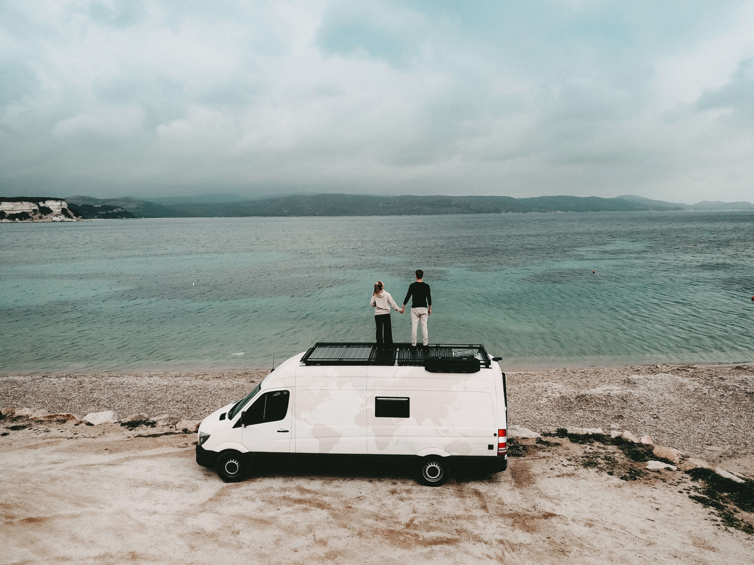 Mann und Frau stehen auf einem Camper am Strand und blicken aufs Meer