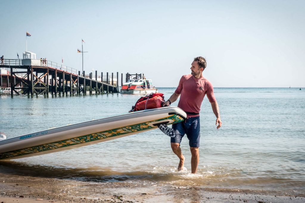 Christo Förster am Strand, wie er ein Stand-Up-Paddle aus dem Wasser hebt