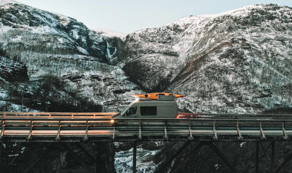 Transporter fährt mit Kajak auf dem Dach über eine Brücke in den Bergen
