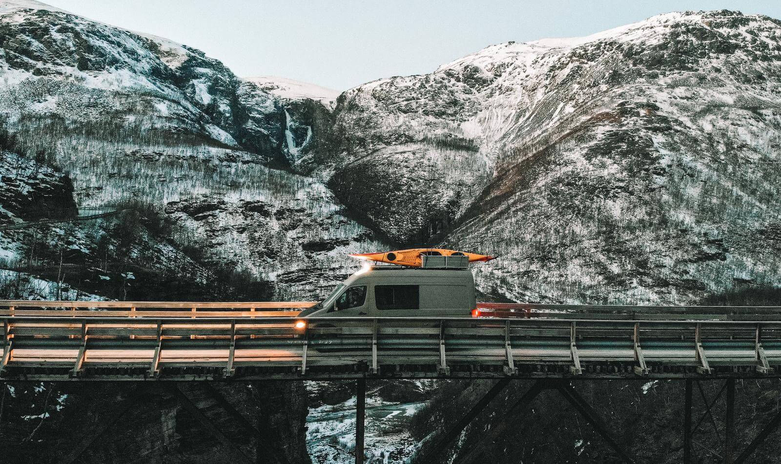 Transporter fährt mit Kajak auf dem Dach über eine Brücke in den Bergen