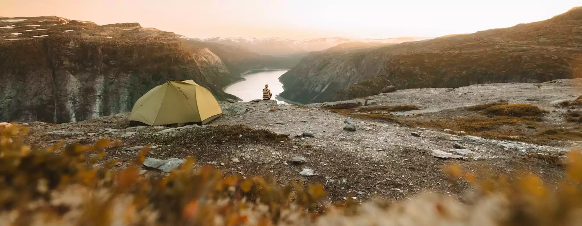 Frau sitzt neben einem Zelt mit blick auf den Fjord in der nähe der Trolltunga in Norwegen