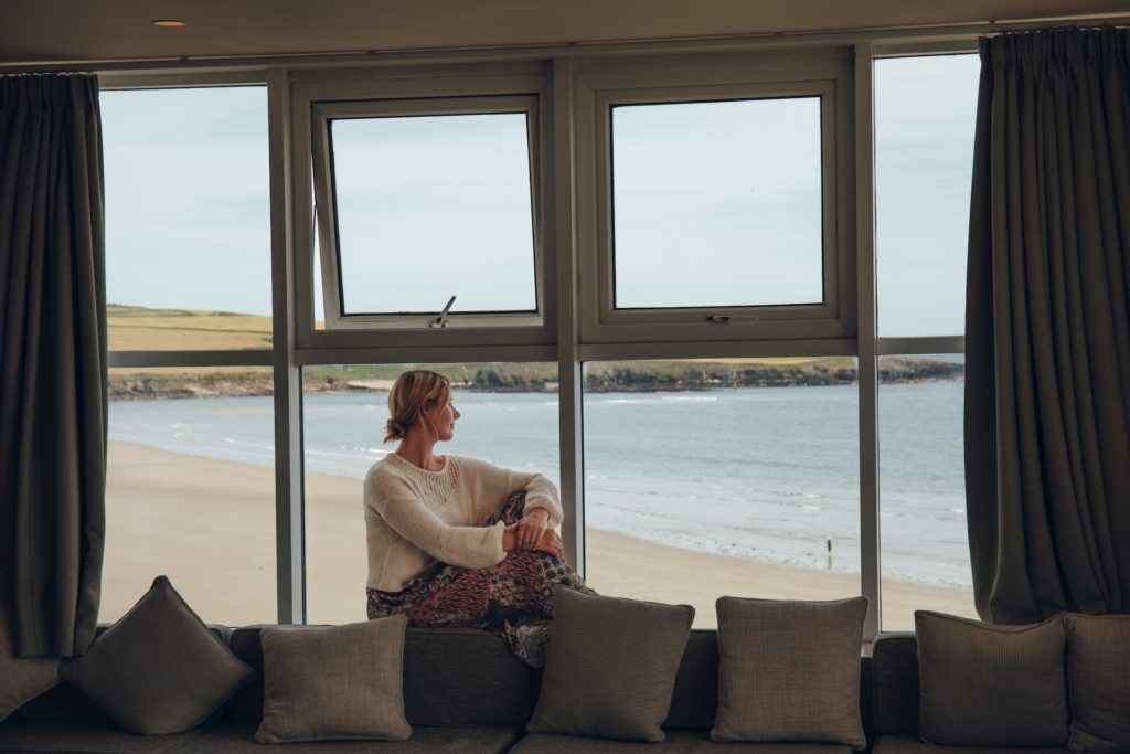 Frau sitzt am Fenster und blickt auf Strand in Irland