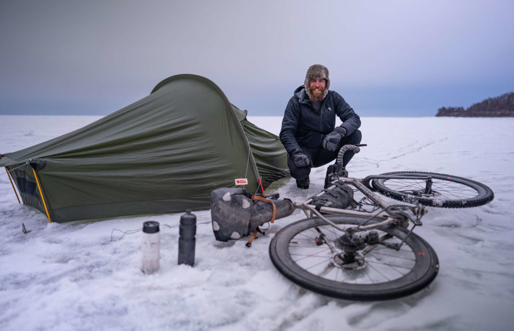 Mann in Schneelandschaft mit Zelt und Fahrrad