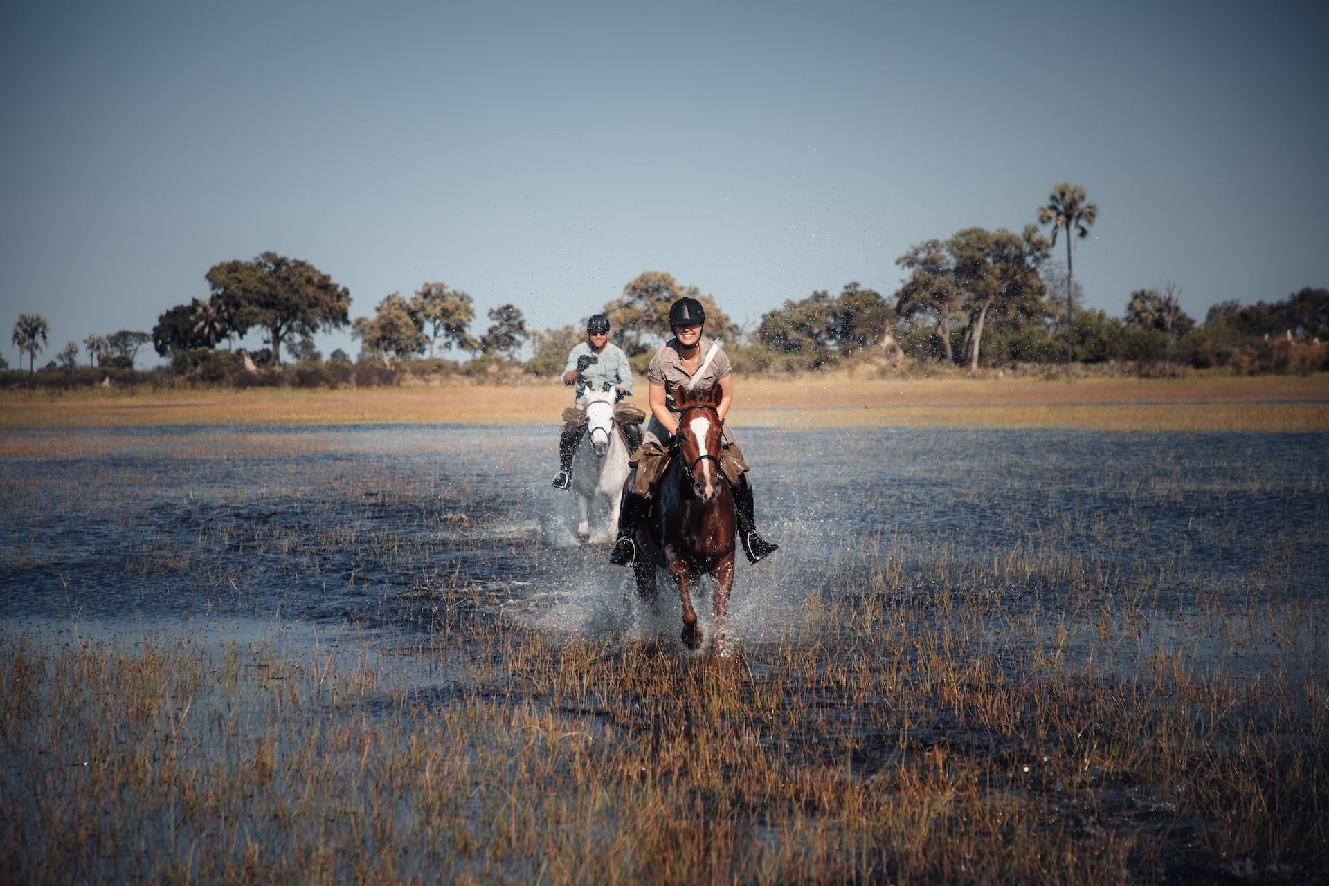 Mann und Frau galoppieren durchs Wasser im Okavango Delta