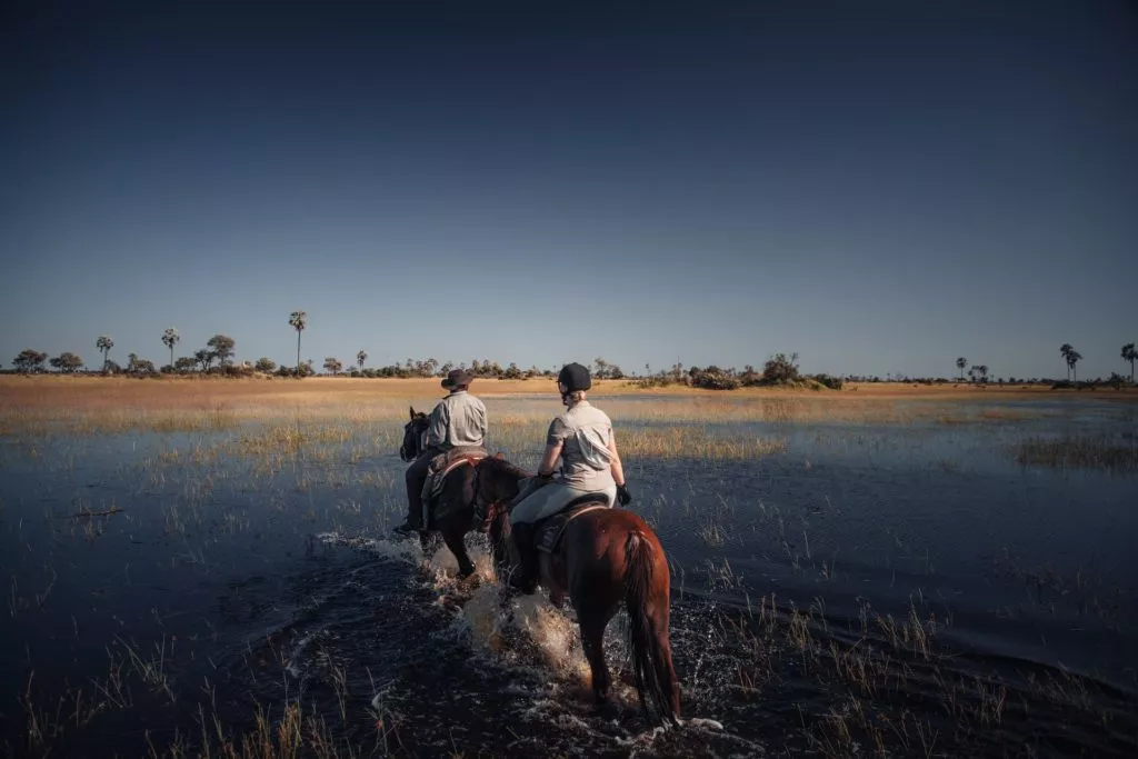 Frau reitet mit Ranger durchs Wasser im Delta Botswanas
