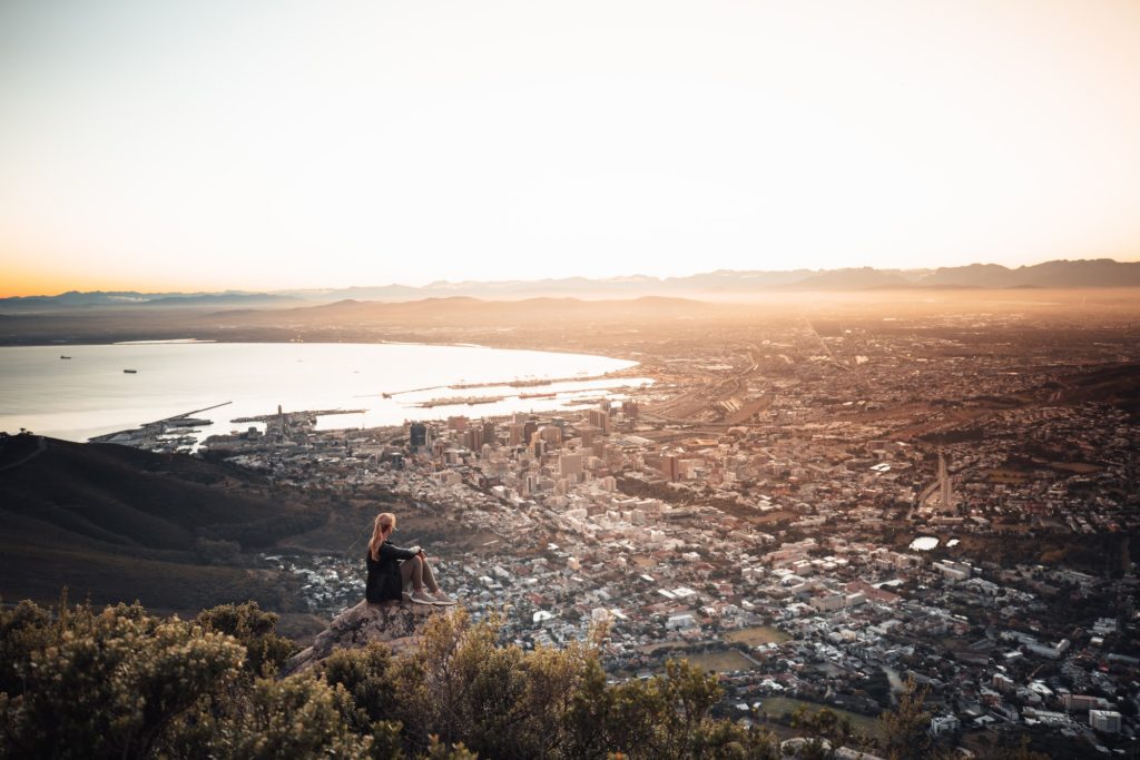 Frau sitzt auf Lionshead zum Sonnenaufang mit Blick auf Kapstadt