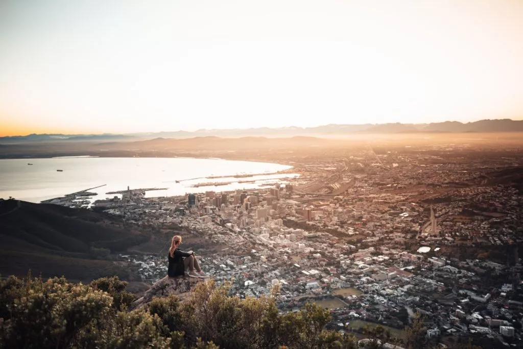 Frau sitzt auf Lionshead zum Sonnenaufang mit Blick auf Kapstadt