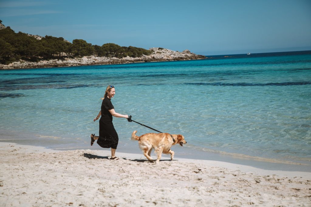 Frau rennt mit ihrem Hund über Strand auf Mallorca
