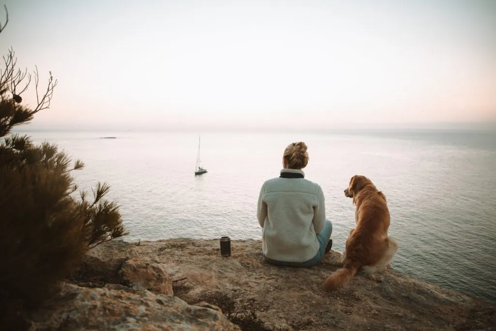 Frau genießt Aussicht auf Meer mit Hund auf Mallorca
