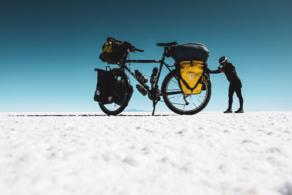 Frau mit einem überdimensional groß erscheinenden Fahrrad auf einem Salzsee in Bolivien