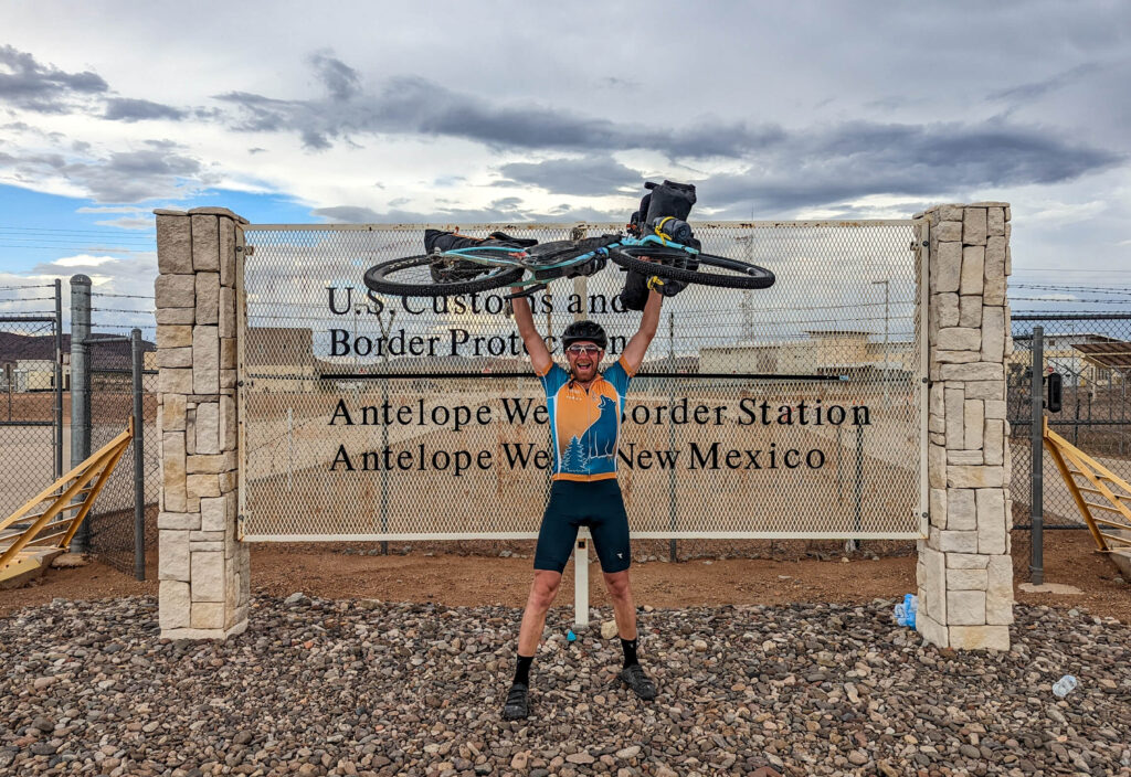 Mann hebt Fahrrad über Kopf am Grenzzaun zu Mexiko