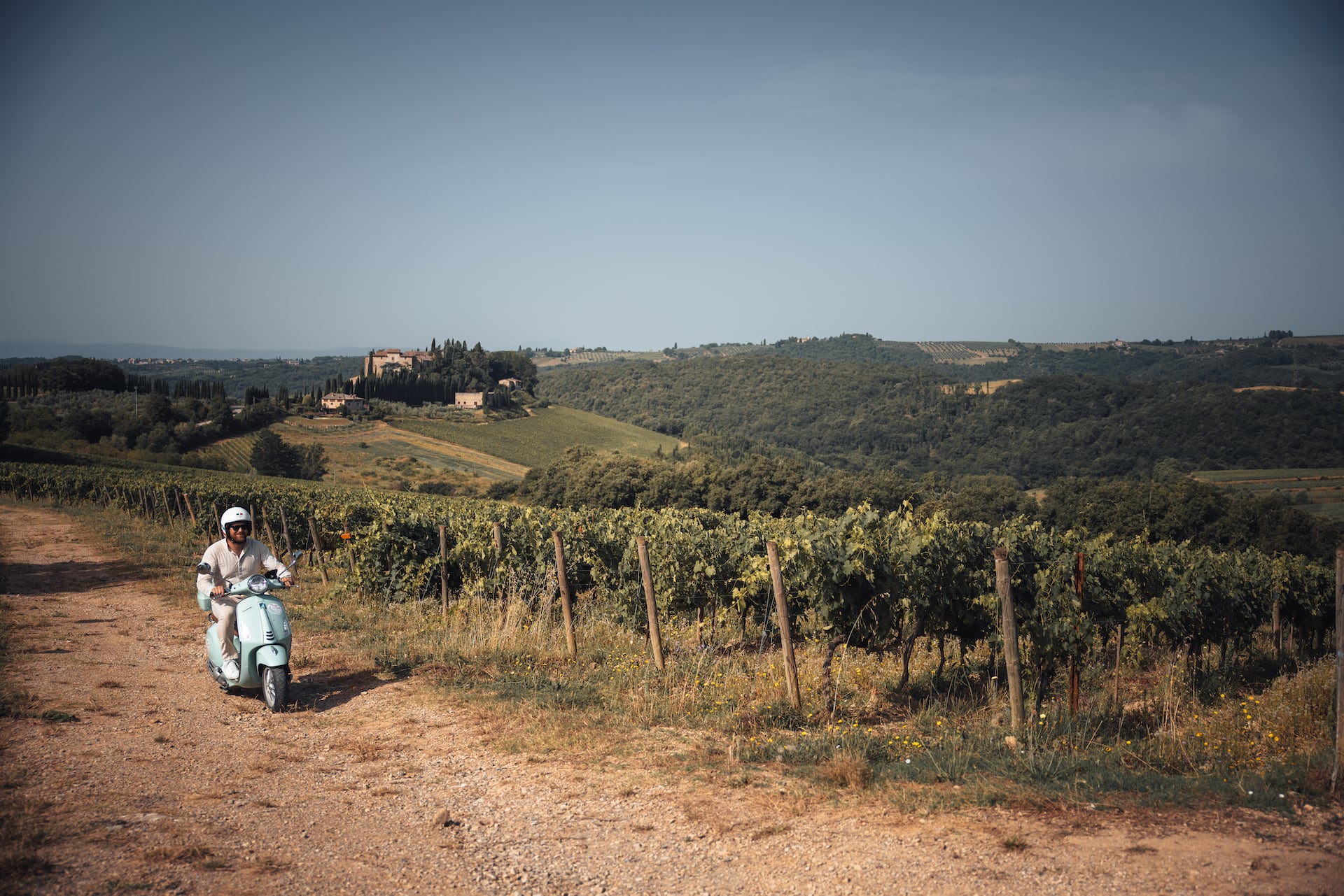 Mann fährt mit einer Vespa durch Weinhügel in der Toskana
