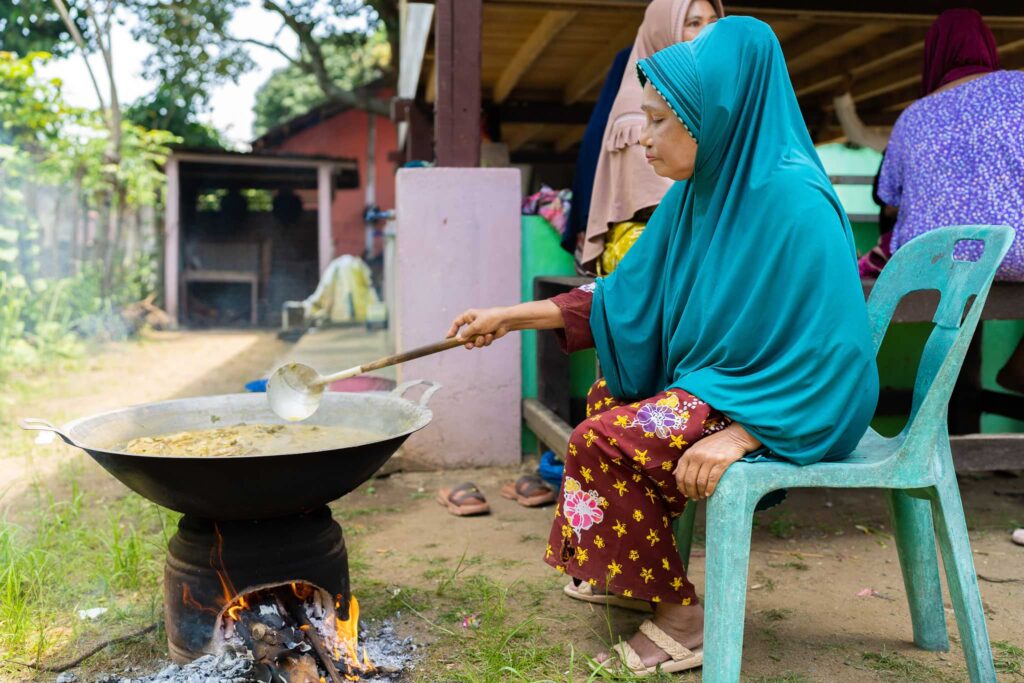 Frau mit Kopftuch kocht Curry im Freien