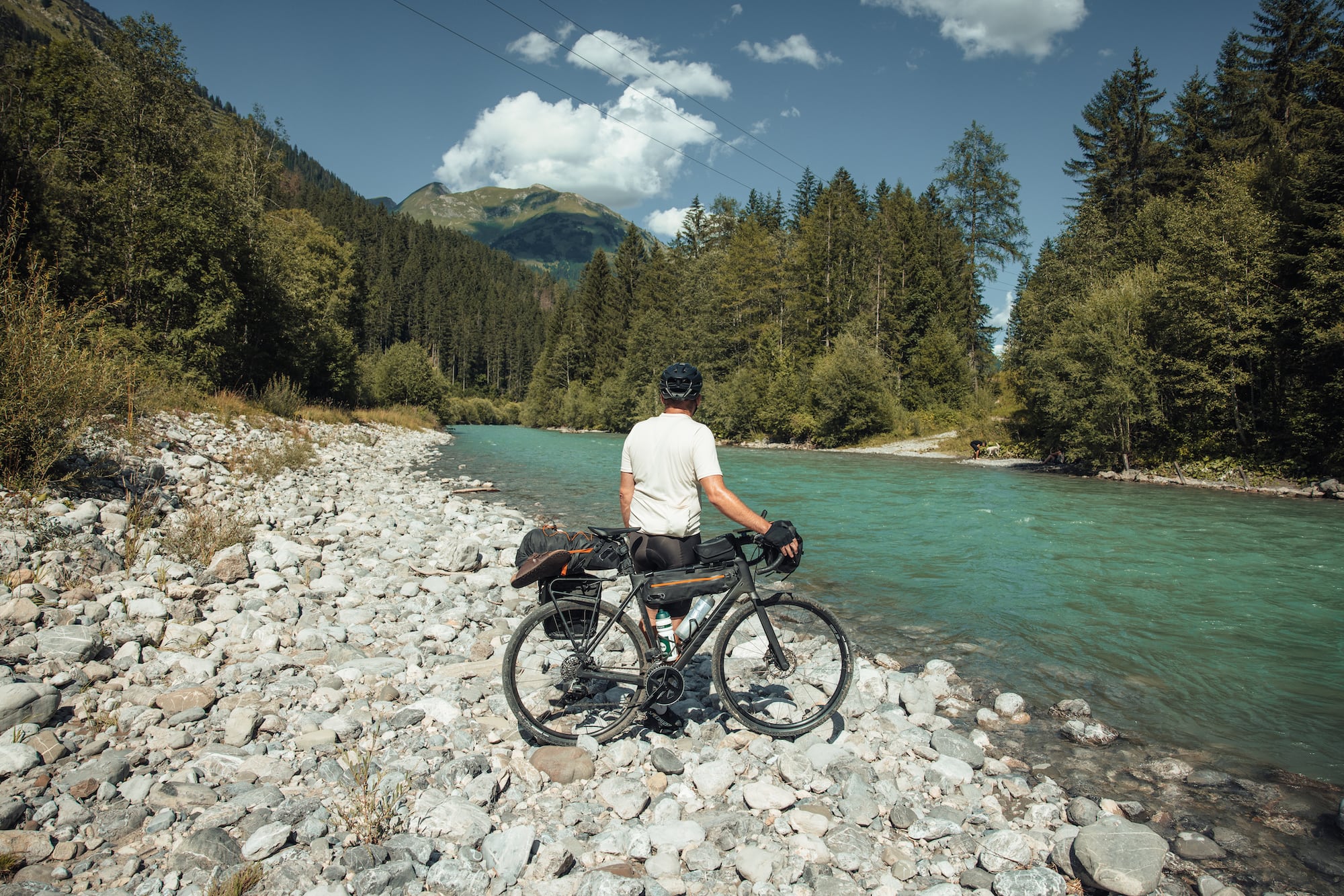 Mann macht Pause am Fluss auf Bikepacking-Tour durch Österreich