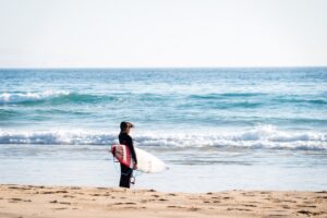 Brückentage Für Deinen Urlaub: Mensch mit Surfbrett am Strand