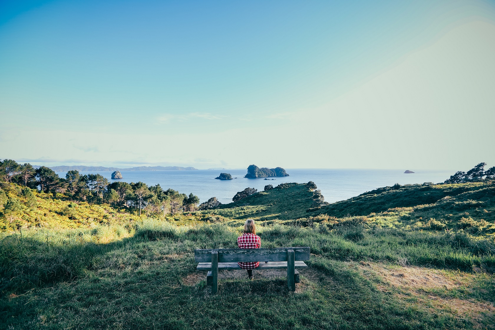 Gut Vorbereitet in den Urlaub: Frau entspannt auf einer Bank mit Blick aufs Meer