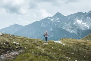 Hüttenwanderung Vorbereitung: Frau wandert mit Rucksack und Wanderstöcken von Hütte zu Hütte durch die Berge