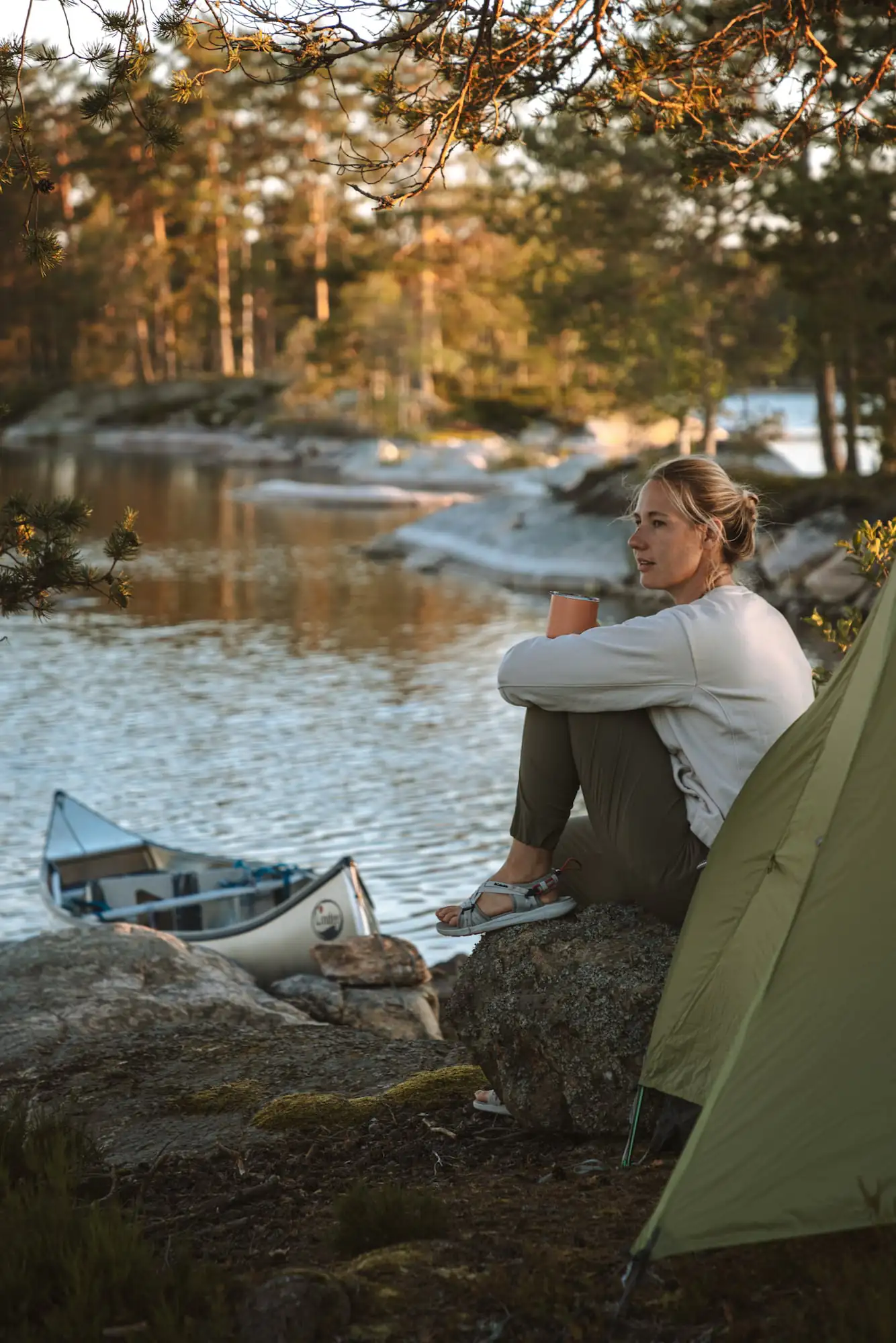 Frische Luft beim Camping: Frau sitzt vor ihrem Zelt am See