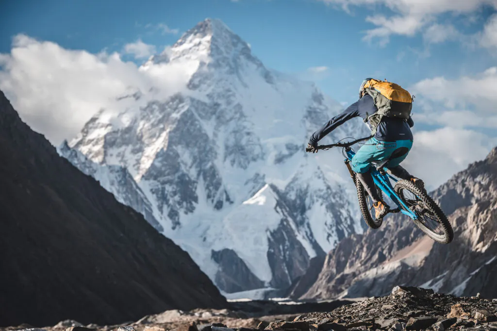 Mann springt auf Mountainbike über Felsen mit Blick auf K2