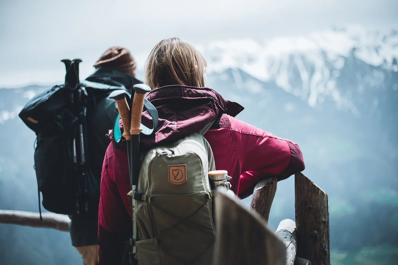 Tour durch die Natur: Wanderer mit Stöcken im Rucksack von hinten schauen auf Berge