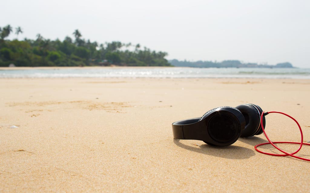 Reise Apps Urlaub: Kopfhörer liegen am Strand