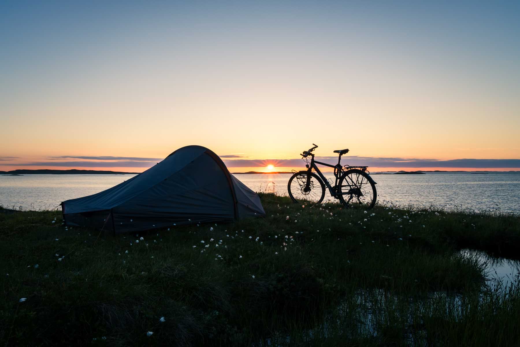 Campingzelt und Fahrrad am Wasser mit Sonnenuntergang