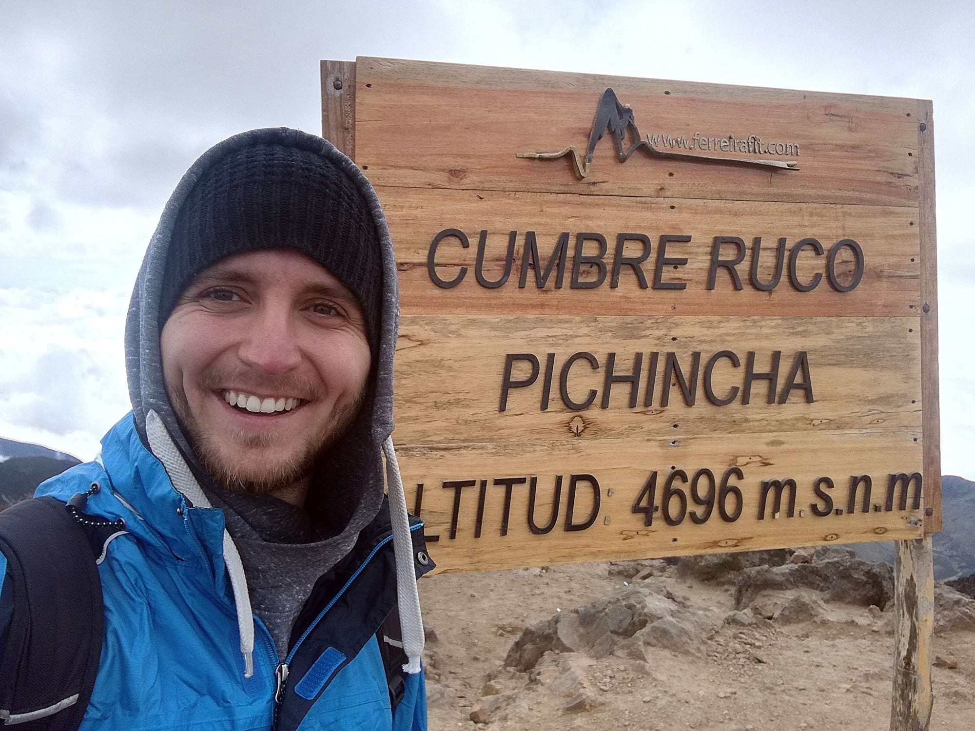 Mann vor einem Schild mit der Aufschrift "Cumbre Ruco Pichinicha 4696 m.s.n.m."