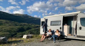 Mann und Frau sitzen vor Campervan im Freien auf Campingstühlen